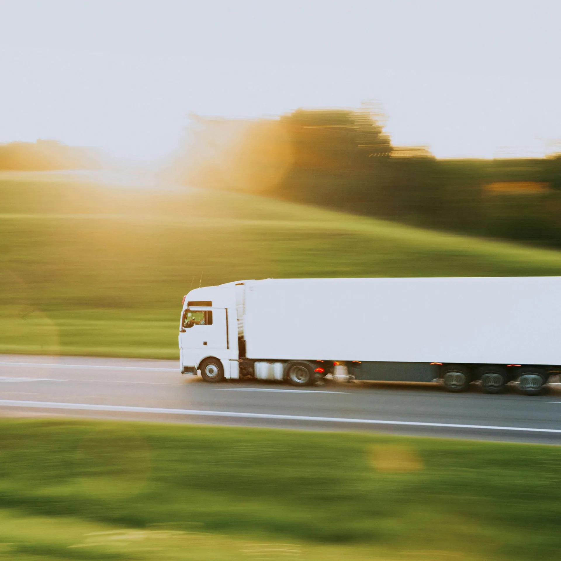 Vit lastbil på väg i grönt landskap